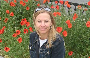 Picture of a woman smiling outdoors with flowers in background.