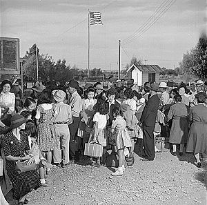 Black and white picture of perhaps 30 people dressed, outdoors, happy, with American flag on pole in background.