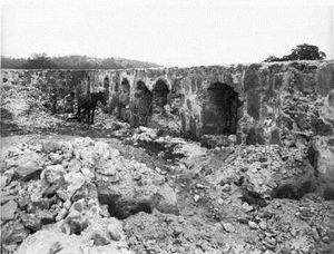 (PD) Photo: C.C. (Charles C.) Pierce Two men remove stones from the ruin of the Santa Margarita de Cortona Asistencia, circa 1906 while a horse hitched to a sledge stands nearby. Five or six arches are visible in the thick stone wall behind the group, and the foreground is littered with stones from the ruin.