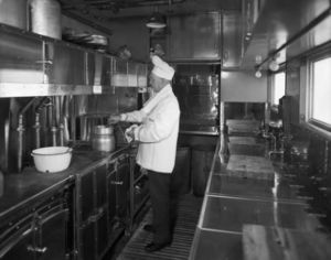 © Photo: George L. Beam / Denver Public Library An interior view of a Denver and Rio Grande Western Railroad dining car kitchen shows a man in a chef uniform stirring a double boiler, surrounded by stainless steel pots, counters, cabinets, sinks, and faucets. The car itself was built in May, 1927 by the American Car and Foundry Company.