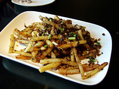A french fry dish served in Beijing, China. The potatoes have been fried, tossed in a spicy low-moisture coating, and topped with scallions.